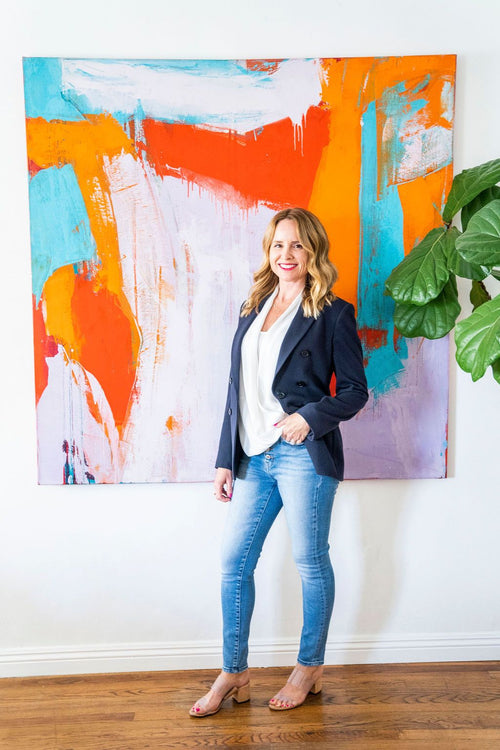 Anna Andrews for fine jewelry standing next to a painting and tree wearing a blue blazer white blouse and jeans