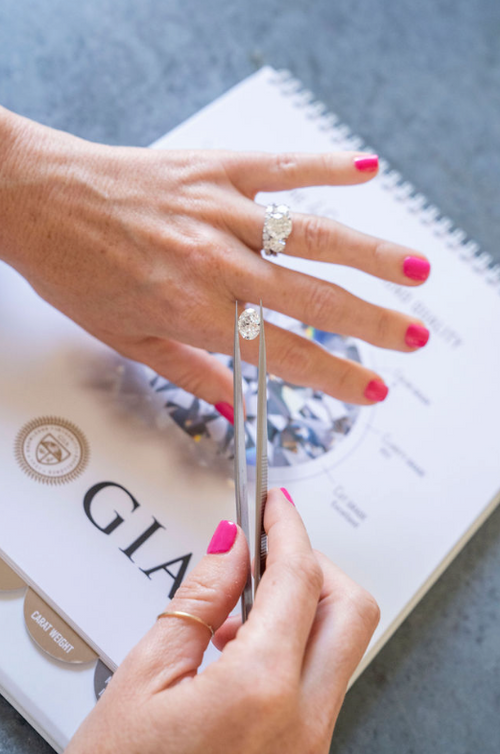 woman with pink nail polish holding stone over hand with diamond ring with large stone over GIA certification document