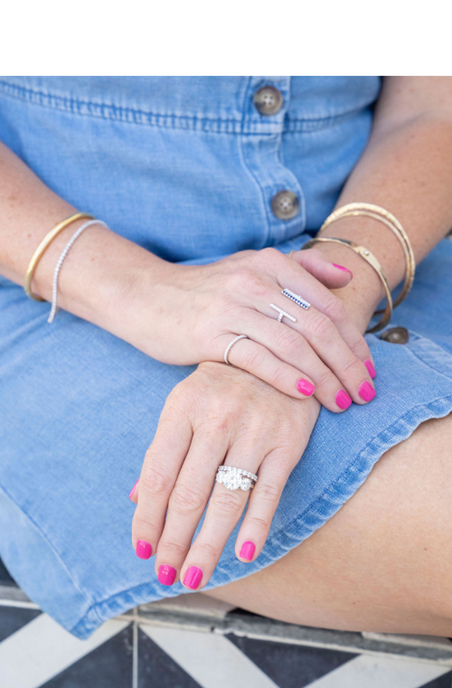 woman in denim dress with hands folded on lap wearing rings and gold bracelets