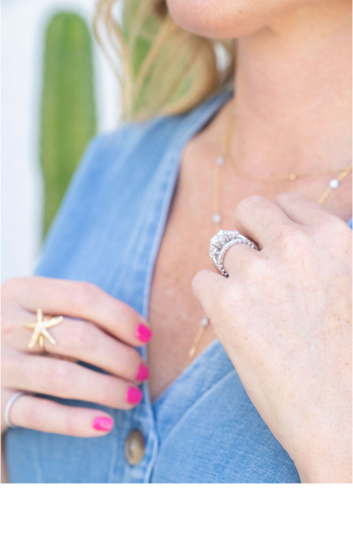 woman in denim dress touching necklace showing diamond ring with large stone and starfish gold ring